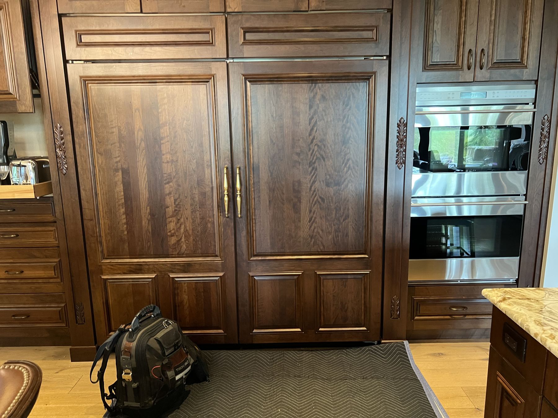 Panel-ready Sub-Zero refrigerator behind wood cabinet doors beside Wolf wall ovens