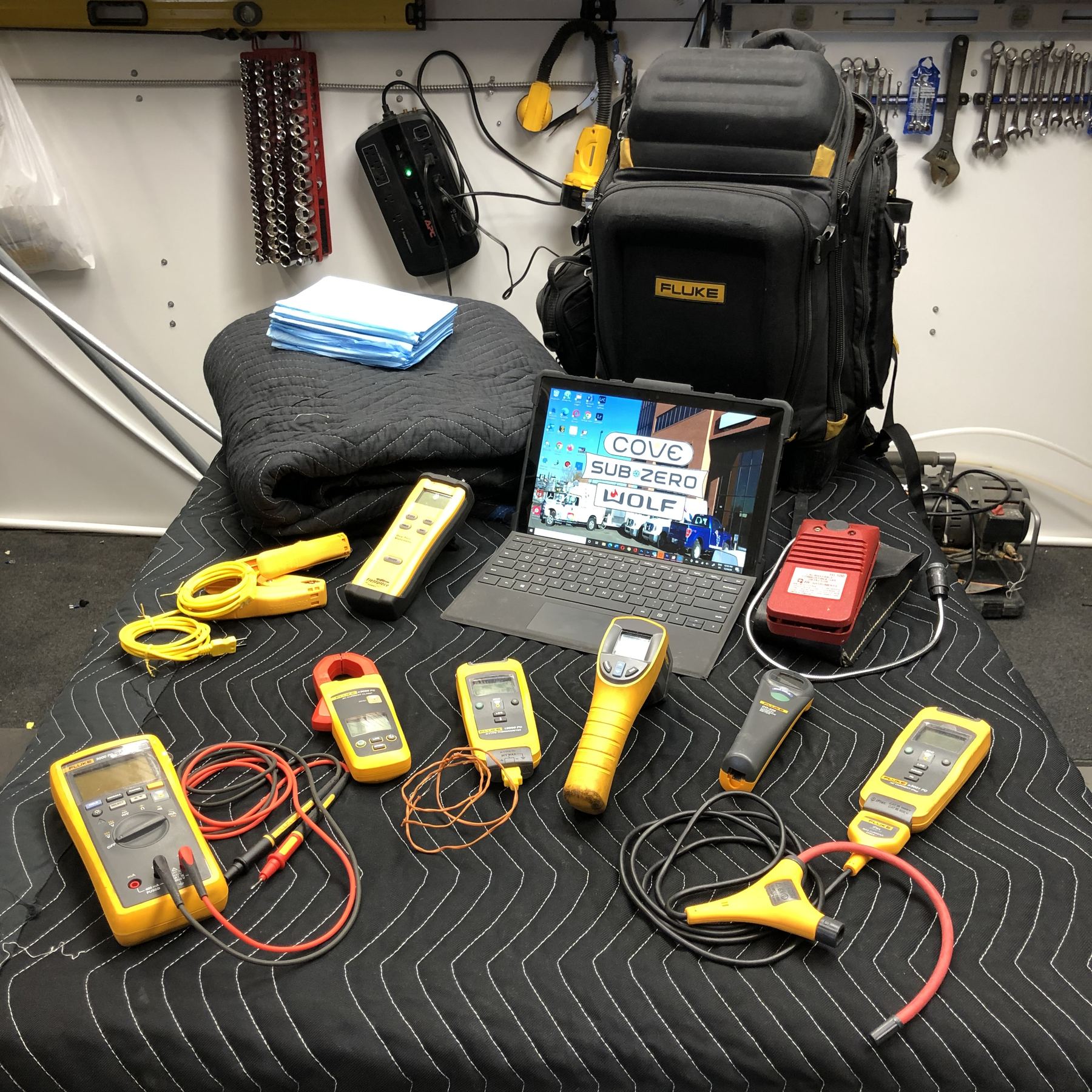 Meters, clamp meters and a diagnostic tablet laid out on a moving blanket